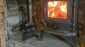A wood-burning stove with a fire burning inside, set in a stone wall. - The Covenanter Hotel (Cupar)