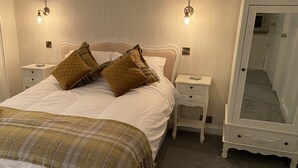 A neatly made bed with two pillows, a bedside table with a lamp, and a full-length mirror. - The Covenanter Hotel (Cupar)