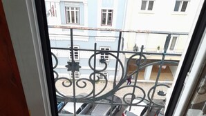 Vista a través de una ventana de un edificio con balcones, que incluye una barandilla metálica y una calle abajo.
