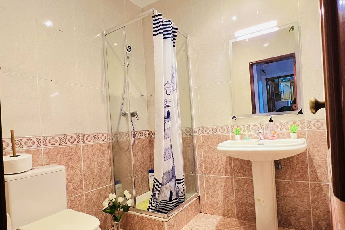 Een badkamer met toilet, douche met glazen deur, wastafel met spiegel en een decoratief vloerkleed.