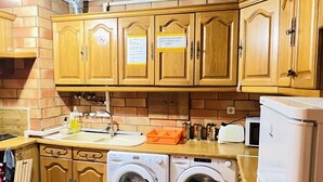 Una cocina con armarios de madera, un lavamanos, un microondas y dos lavadoras.