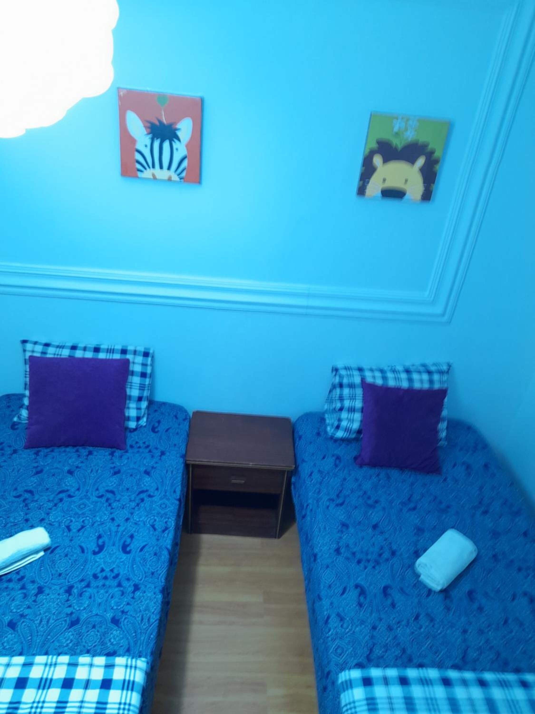 Une chambre avec deux lits, chacun recouvert d’une courtepointe bleue à motifs et agrémenté d’oreillers assortis. Une petite table de chevet en bois se trouve entre les deux lits.