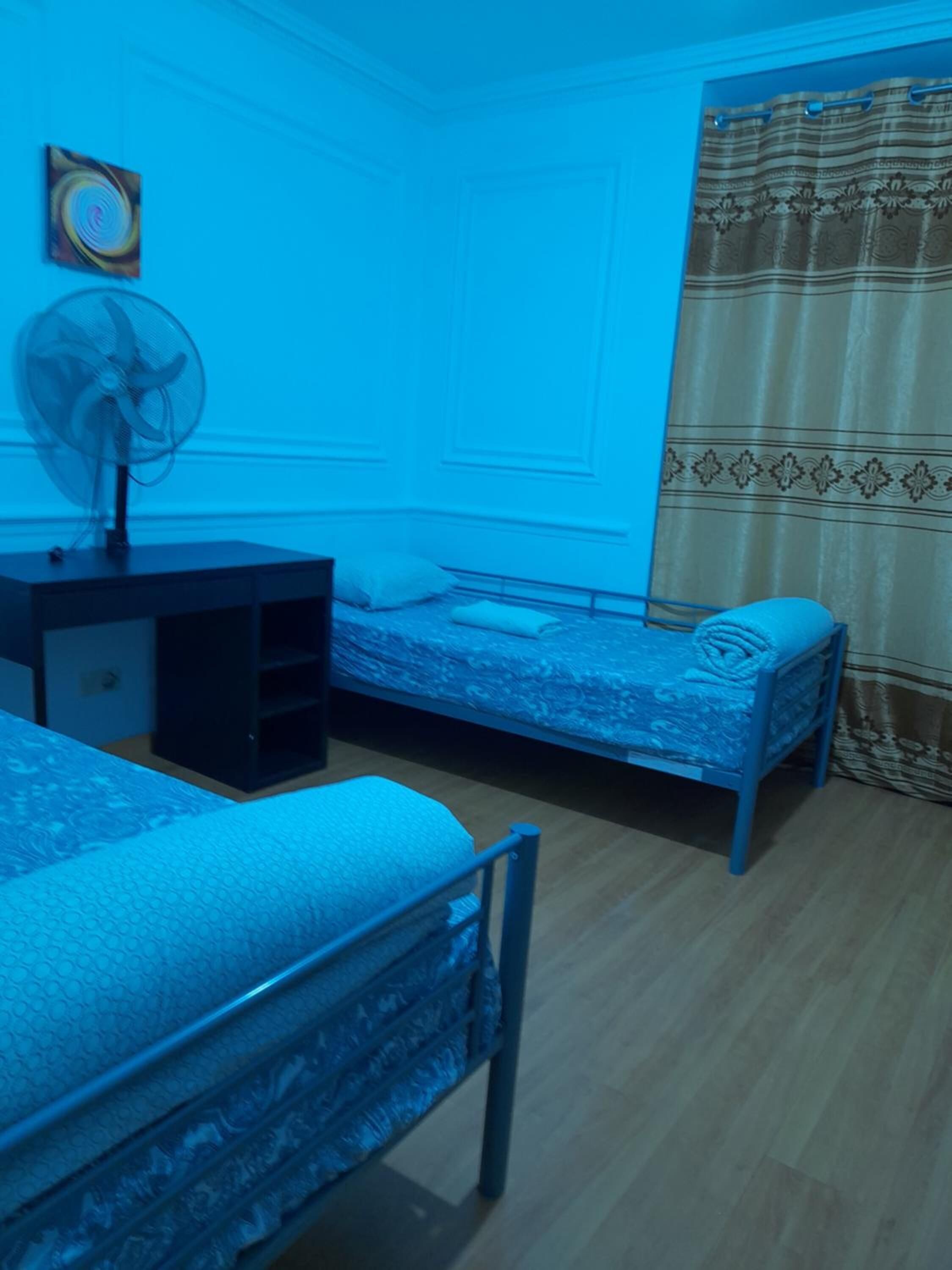 A bedroom with two beds, a desk, a chair, a fan, and a curtain.