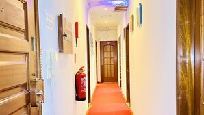 Un pasillo de hotel con alfombra roja, puertas de madera y un extintor de incendios fijado en la pared.