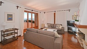 Una sala de estar con sofá, una mesa de centro, televisor y un balcón con vistas.