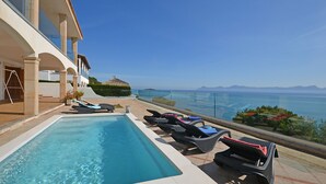 Una piscina con sillas de descanso, barandilla de cristal y vista al mar.