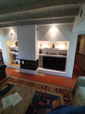 A living room with a fireplace, shelves with decorative items, a television, and a patterned rug.