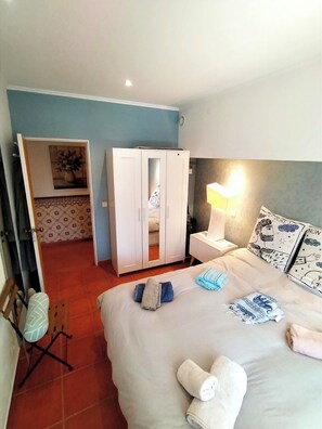 A hotel room with a bed, a wardrobe, a bedside table with a lamp, and a wall with a poster.