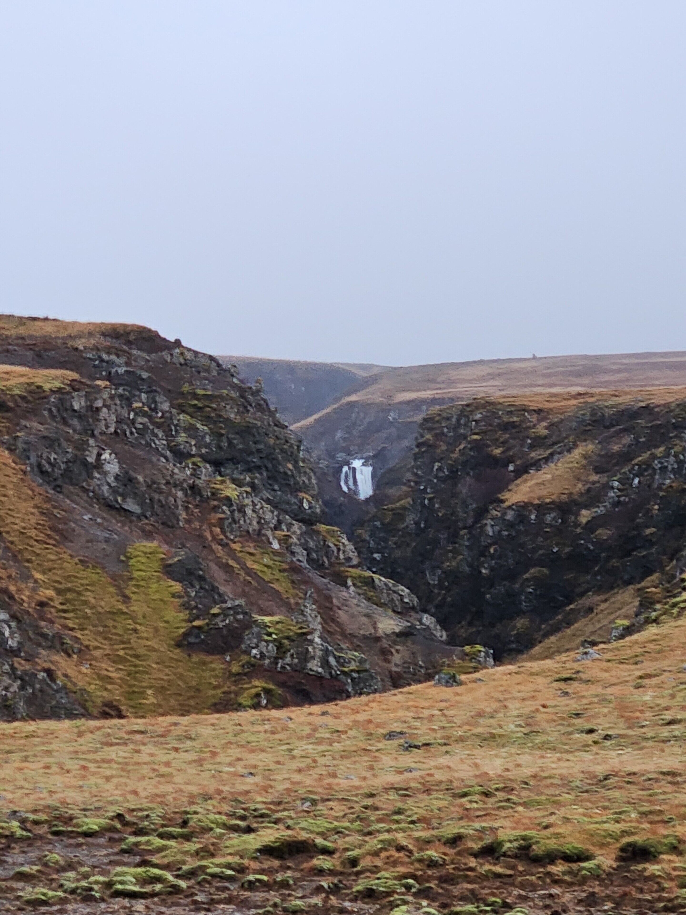 A rugged landscape with a waterfall in a canyon.