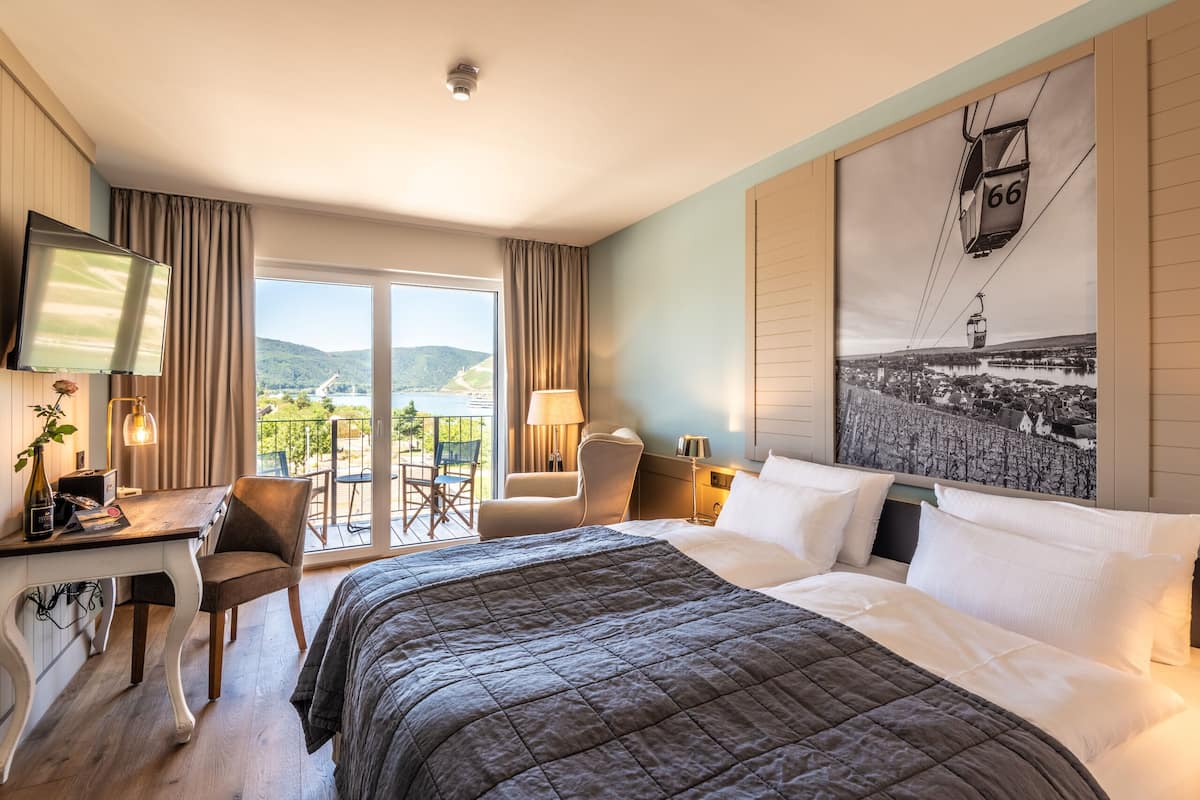 Une chambre d’hôtel avec un grand lit, un bureau avec une chaise, une télévision et un balcon offrant une vue sur les montagnes.