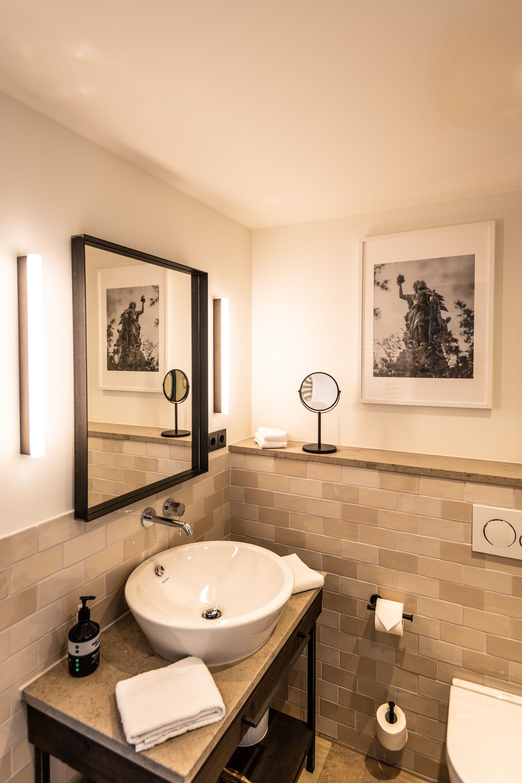 Ein Badezimmer mit einem großen Spiegel, einem Waschbecken, einer Toilette und einem gerahmten Bild an der Wand.