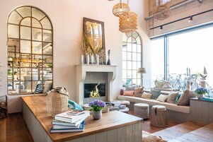 A cozy living room with a fireplace, wooden furniture, and large windows offering a view of bicycles outside.