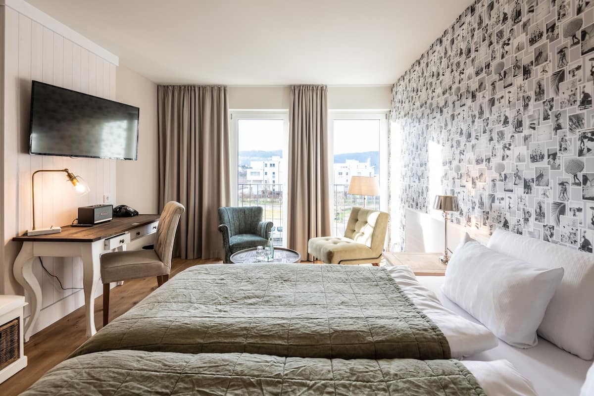 Une chambre d’hôtel avec un lit, un bureau avec un ordinateur, une chaise, une télévision et un mur décoré de photos.
