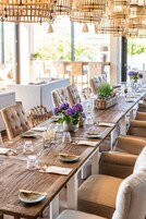 A long dining table with chairs, a vase of flowers, and a basket of plants.