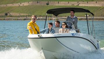 A boat with four people on board, moving on a body of water with a hilly landscape in the background.