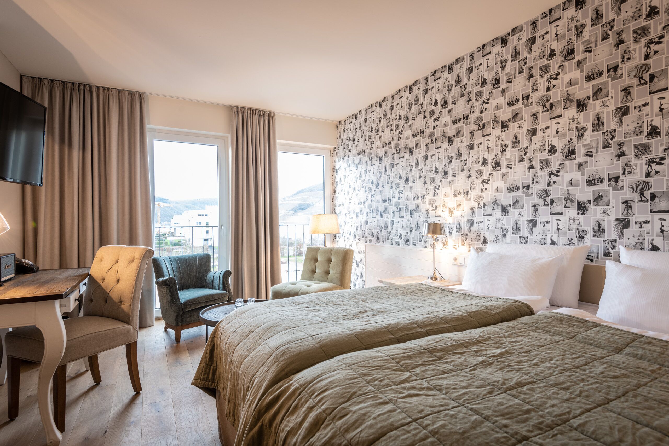 A hotel room with a large bed, a desk, a chair, and a wall covered with black and white photos.