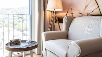 Ein modernes Zimmer mit Blick auf die Stadtlandschaft, ein runder Holztisch mit Zeitschrift und Gläsern, ein beiges Sofa mit dekorativem Text und eine Stehlampe.