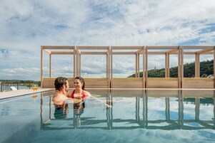 A clear swimming pool with a wooden deck and a view of a natural landscape.