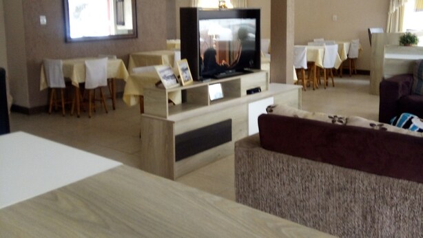 A modern living room with a flat-screen TV, wooden furniture, and a dining area with tables and chairs. - Hotel Santa Rita (Capao da Canoa)