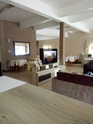 A modern living room with a flat-screen TV, wooden furniture, and a dining area with tables and chairs. - Hotel Santa Rita (Capao da Canoa)