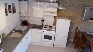 A compact kitchen with white cabinets, a built-in oven, a gas stove, and a sink. There are three pendant lights above the counter.