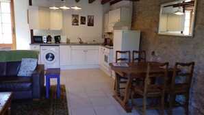 A compact kitchen with white cabinets, a washing machine, and a dining area with a wooden table and chairs.