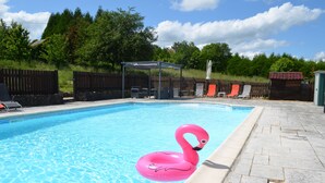 A swimming pool with a pink flamingo float, lounge chairs, and a covered seating area.