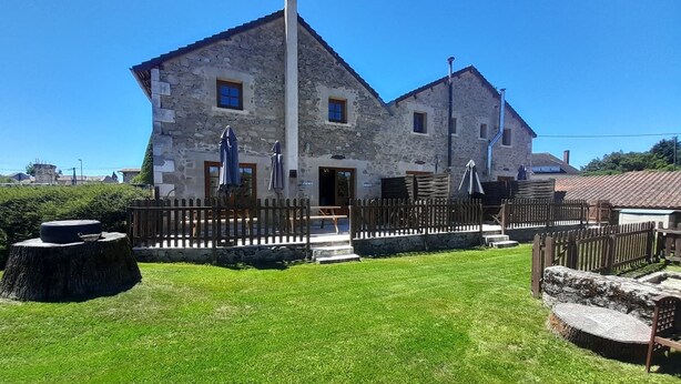 A stone building with a wooden fence, a grassy lawn, and a picnic table.