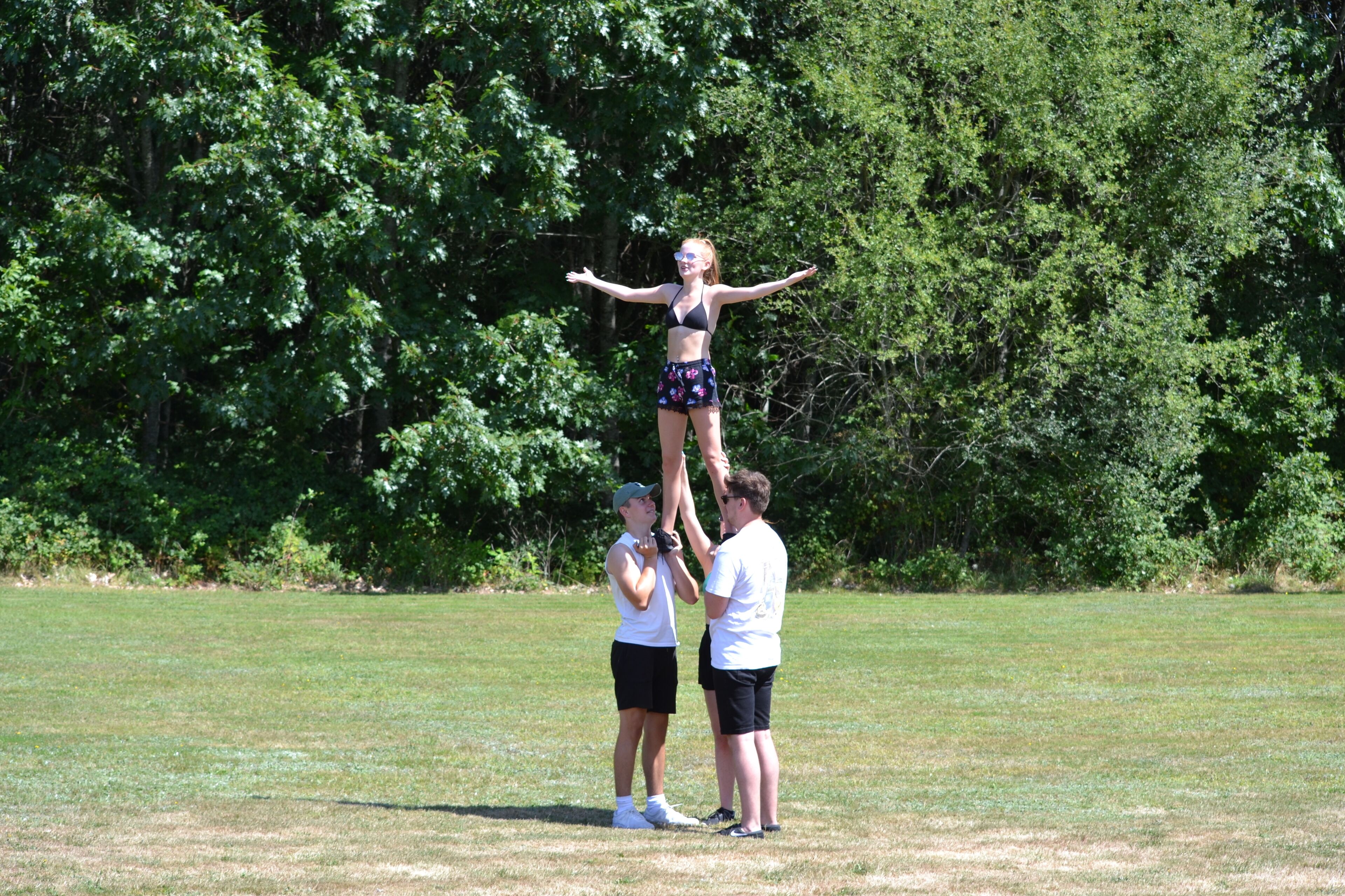 A group of people performing a cheerleading stunt in an open field with trees in the background.