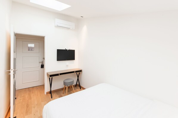 Une chambre avec un lit, un bureau, une chaise et un téléviseur fixé au mur.