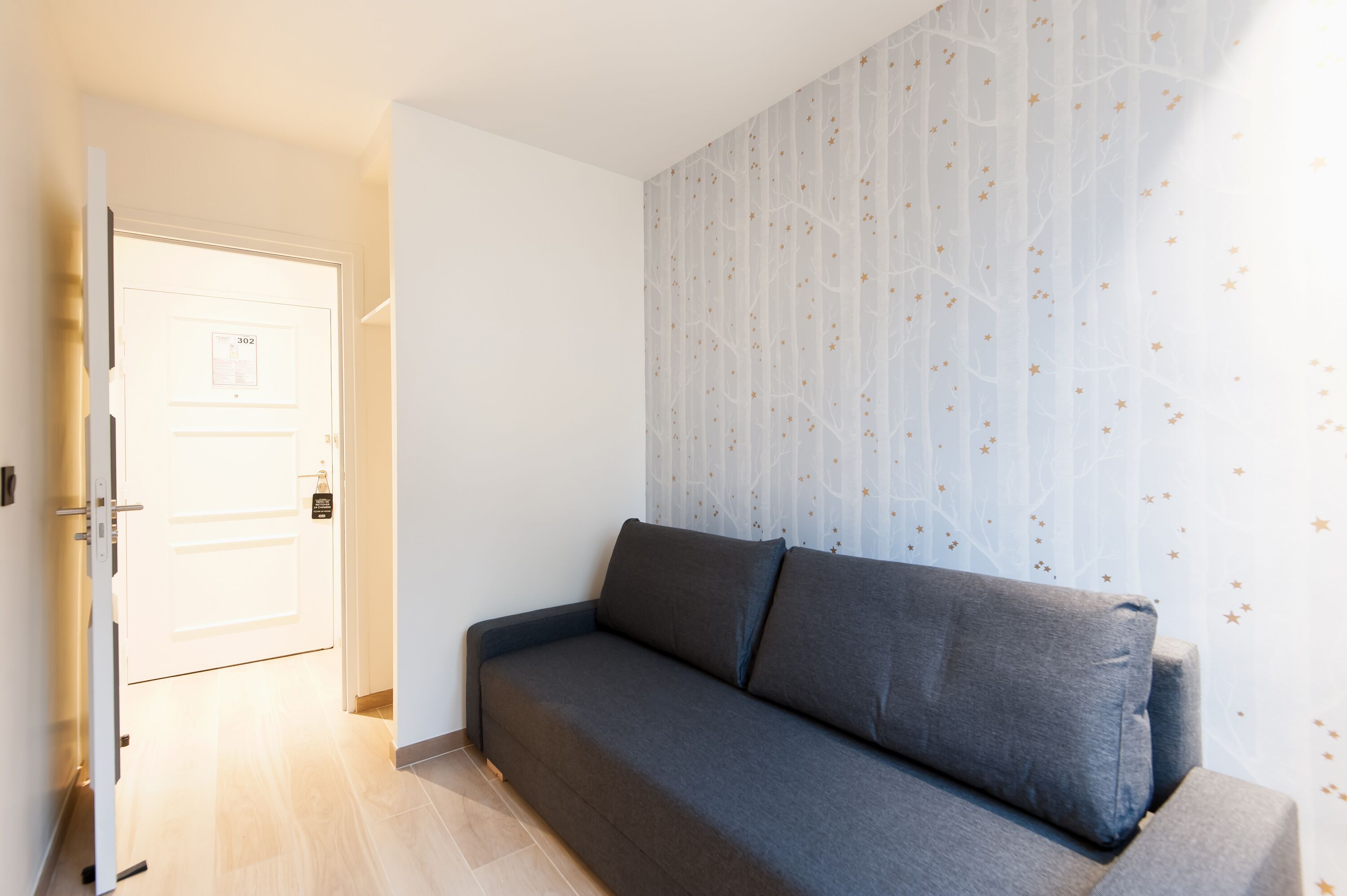 Una habitación con un sofá gris, una puerta con un número y una pared con un motivo de árbol.