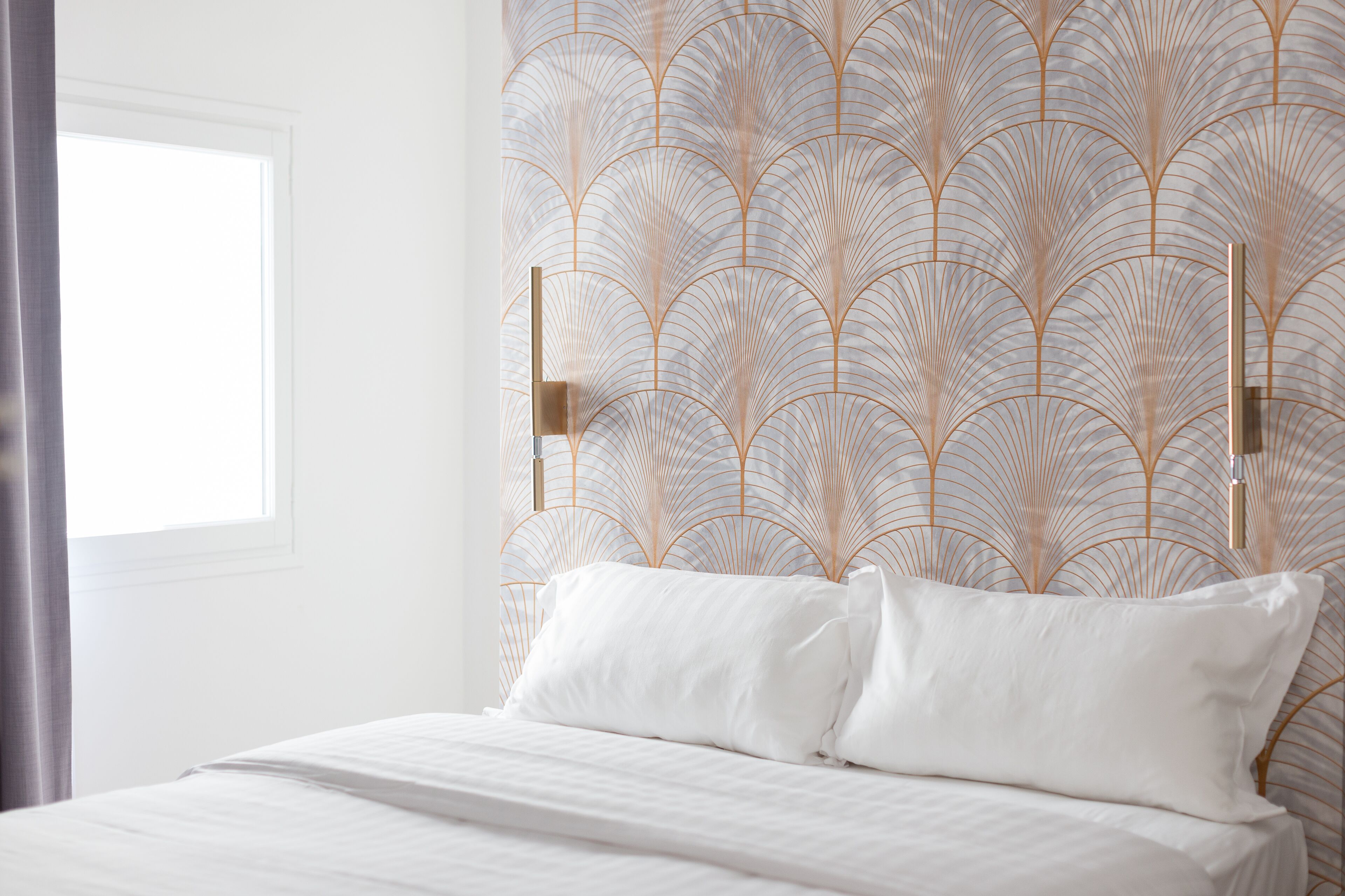 Een net opgemaakt bed met witte lakens en een hoofdbord met een decoratief patroon.