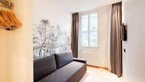 Una sala de estar moderna con un sofá gris, un televisor montado en la pared y una ventana con cortinas.