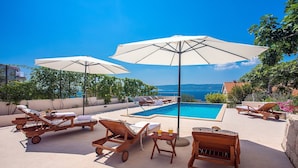 A poolside area with lounge chairs, umbrellas, and a view of the sea. - Villa Dasianda - only 90 m from the beach, private 30msq heated pool (Stanici)