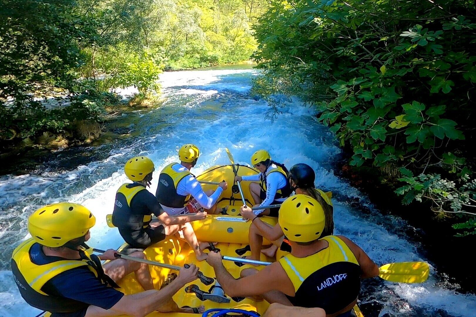 Een groep mensen in een gele rubberboot die over een rivier vaart, omringd door dichte begroeiing.