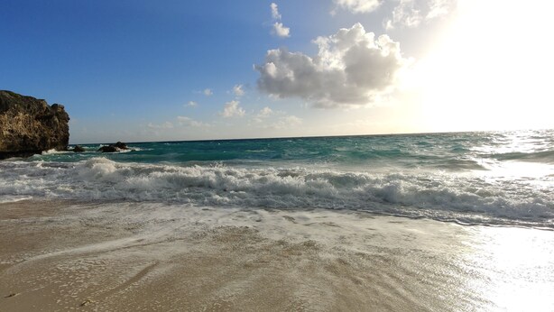 Ein Strand mit Wellen, einem felsigen Felsen und blauem Himmel.
