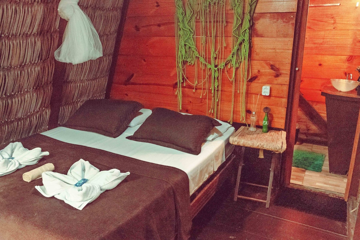 Una habitación de madera con una cama, toallas, una lámpara colgante y una mesita con un cuenco.