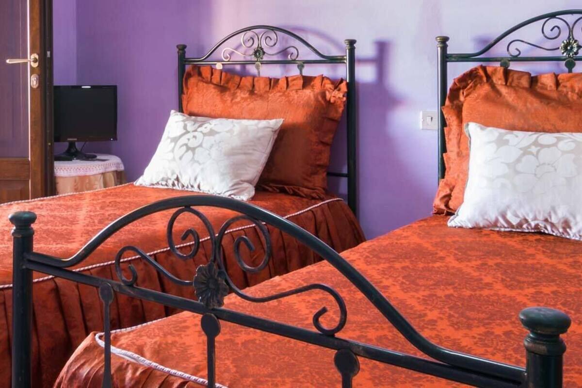 Two beds with black metal frames and orange bedding in a room with purple walls.