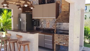 Eine Küche mit Einbauofen, Kühlschrank und Kaffeemaschine. Zwei hölzerne Barhocker und ein Fenster mit Blick auf einen Garten.