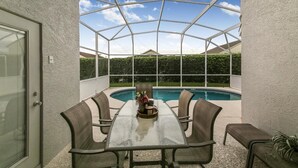 Une terrasse couverte avec une table et des chaises en verre, une piscine et une vue sur le jardin arrière.