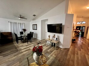 Un salon moderne comprenant un coin repas, un téléviseur à écran plat fixé au mur et un ventilateur de plafond.