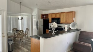 Une cuisine moderne avec des meubles en bois, un réfrigérateur en acier inoxydable, un four à micro-ondes et un coin repas comprenant une table et des chaises en verre.