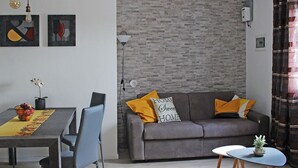 Una sala de estar moderna con un sofá gris, dos almohadas amarillas, una mesita y una mesa de comedor con sillas.