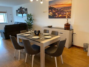 Comedor con mesa de madera dispuesta para cuatro, rodeada de sillas, un sofá y una planta en maceta.