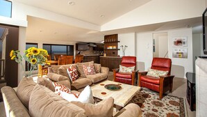 A spacious living room with a sofa set, a coffee table, and a red leather armchair. A kitchen is visible in the background. - Paradise Awaits - Panoramic Ocean Views, big space (Solana Beach)
