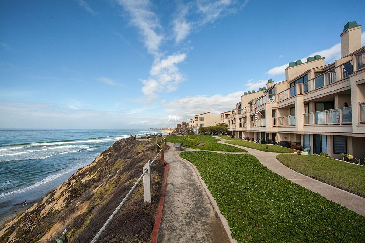 A coastal hotel with a pathway leading to the beach, featuring balconies and a view of the ocean.