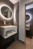 Ein modernes Badezimmer mit einem großen, ovalen Spiegel, einem weißen Waschbecken und einem Handtuchhalter.
