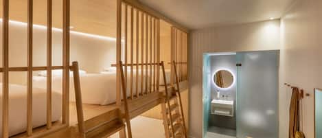 A hotel room with a bunk bed, a small bathroom with a mirror, and a wooden ladder.