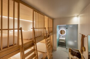Ein Hotelzimmer mit Etagenbett, einem kleinen Badezimmer inklusive Spiegel und einer Holzleiter.