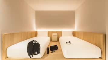 A compact room with two single beds, a small table, a backpack, and a suitcase.